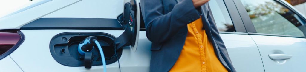 why transition your business to EV - a close up of a business woman in an orange shirt and navy blazer, leaning against a silver electric car