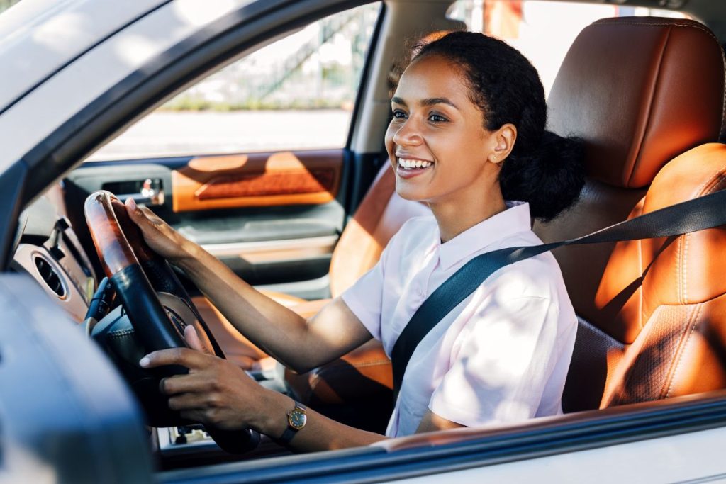 A closeup of a young, smiling woman driving and electric car